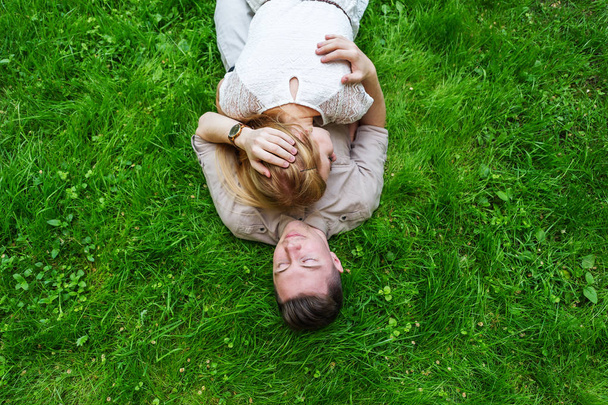 Beautiful young couple lying on the bright green grass. Spring nature. Lifestyle, leisure concept. Outdoor portrait  - Photo, image