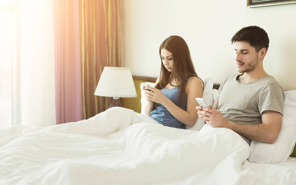 Молода пара використовує свій мобільний телефон у ліжку ігноруючи один одного
 - Фото, зображення