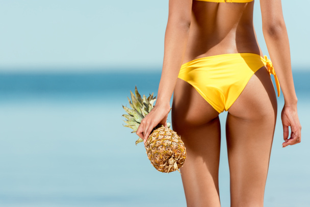 cropped image of woman in bikini holding pineapple in front of sea  - Fotografie, Obrázek