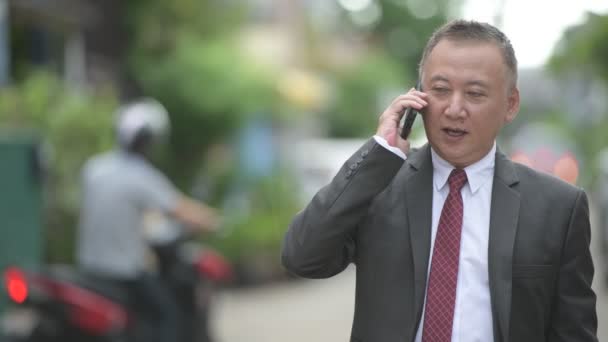 Mature Japanese businessman using phone in the streets outdoors - Footage, Video