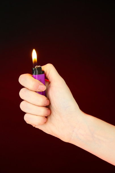 Burning lighter in female hand, on dark red background - Foto, afbeelding