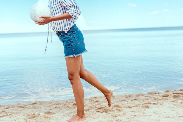 обрезанное изображение женщины, держащей мяч для пляжного волейбола перед морем
  - Фото, изображение