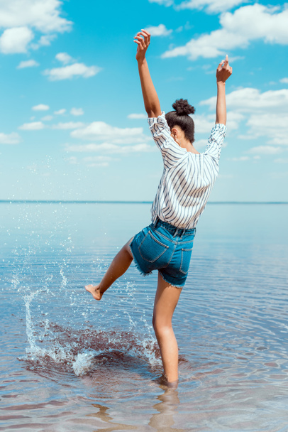 vista trasera de mujer joven con brazos anchos pateando agua de mar
  - Foto, Imagen