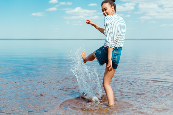 happy african american woman kicking sea water  - 写真・画像