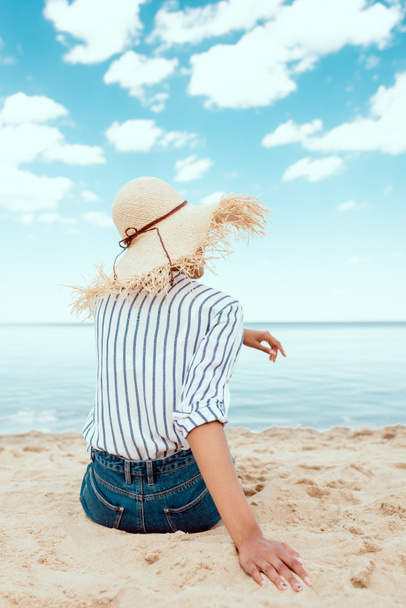 vue arrière de la femme en chapeau de paille assis sur la plage de sable
  - Photo, image