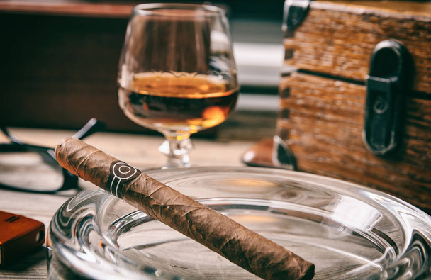 Cubaanse sigaar en een glas cognac brandy op houten achtergrond, close-up weergave met details - Foto, afbeelding