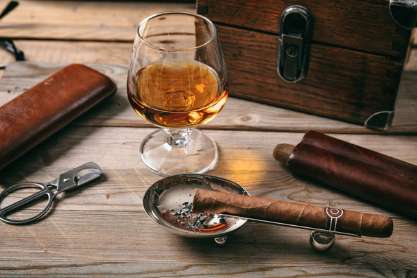 Cuban cigar and a glass of cognac brandy on wooden background, closeup view - Fotó, kép
