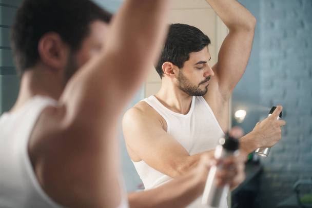 Hombre usando desodorante de aerosol en axila para mal olor
 - Foto, Imagen