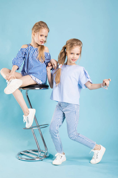 Tytöt kaksoset vaaleansinisissä vaatteissa poseeraavat baarijakkaran lähellä sinisellä pohjalla
. - Valokuva, kuva