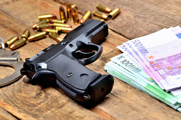 Pistola da 9 mm - pistola, manette, proiettili e banconote in euro su un vecchio tavolo di legno
 - Foto, immagini