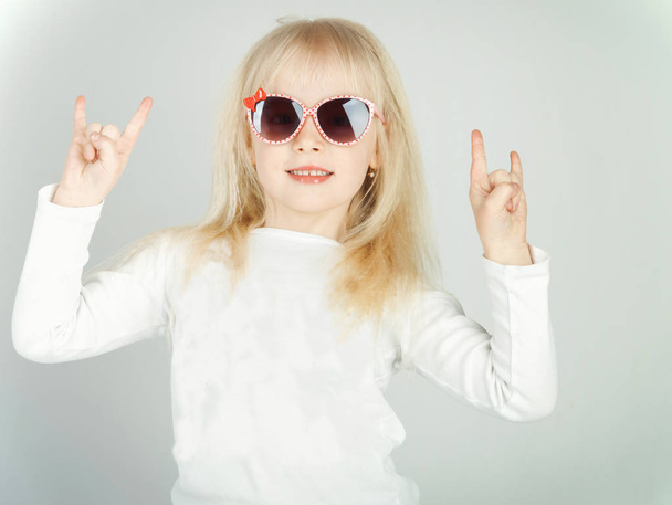 little girl in a fashionable blouse and pink glasses, making her face and happy. toned photo - Foto, afbeelding
