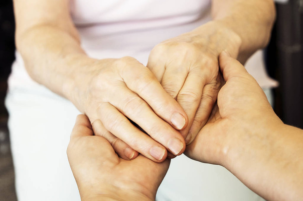 Mature female in elderly care facility gets help from hospital personnel nurse. Senior woman w/ aged wrinkled skin & care giver, hands close up. Grand mother everyday life. Background, copy space. - Photo, Image