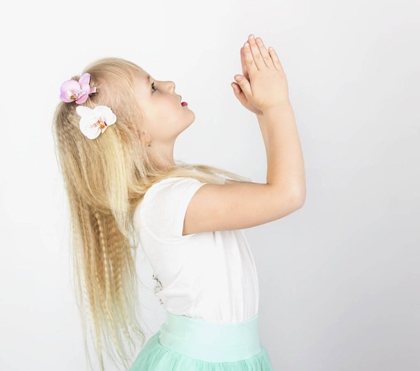 little blond girl folded her hands in prayer to God. A little angel. Side view - Photo, image