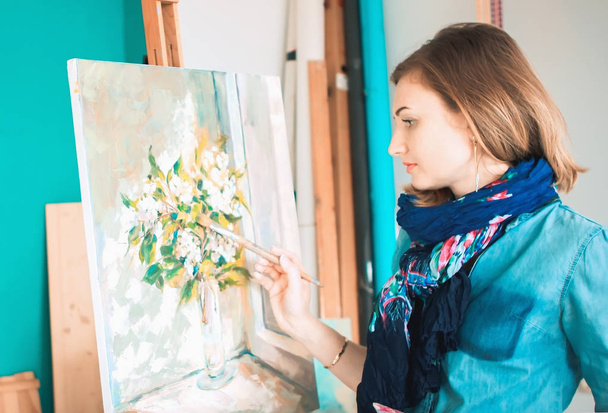 portrait of a girl painter with a palette of colorful paintings in an art studio. Thoughtful artist, creative mood - 写真・画像