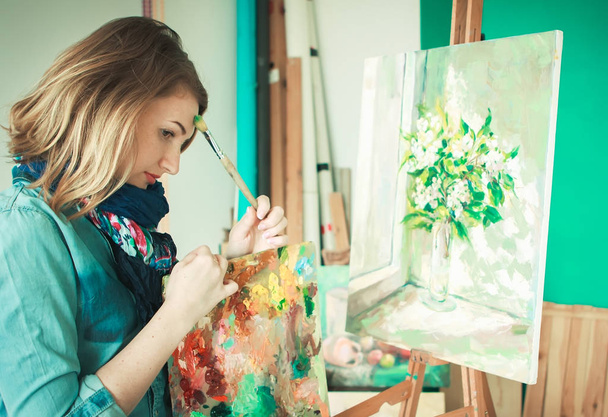 portrait of a girl painter with a palette of colorful paintings in an art studio. Thoughtful artist, creative mood - Foto, afbeelding
