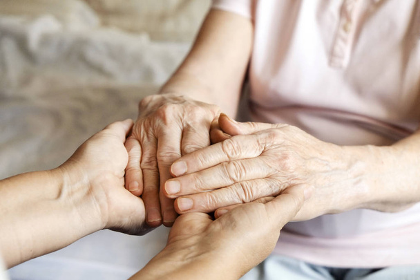 Mature female in elderly care facility gets help from hospital personnel nurse. Senior woman w/ aged wrinkled skin & care giver, hands close up. Grand mother everyday life. Background, copy space. - Foto, imagen