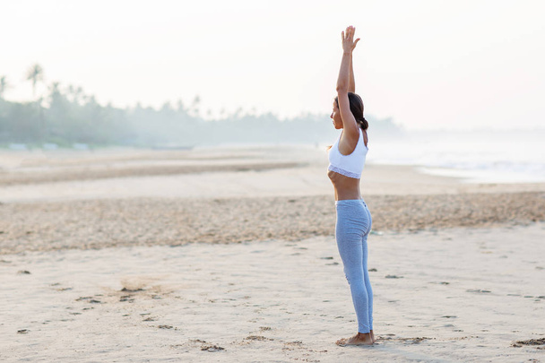 Caucasian woman practicing yoga at seashore of tropic ocean - Фото, изображение