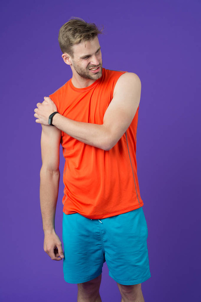 Sportsman touch shoulder on violet background. Muscular man feel pain after training or workout. Pain in shoulder. Sport injury. I need massage. Health care and treatment. Bodycare and wellness - Fotoğraf, Görsel