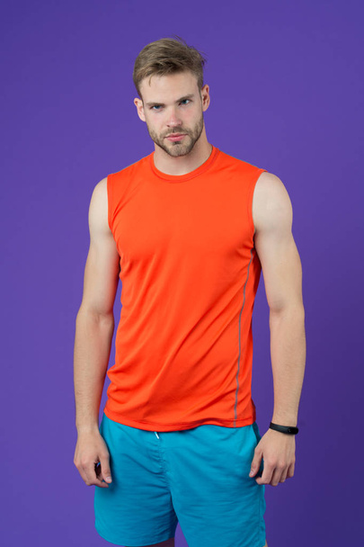 Sportsman on violet background. Muscular man in orange vest and blue shorts. Fit and confident. Sport fashion for training and workout. Personal trainer for healthy lifestyle. Fitness and wellness. - Zdjęcie, obraz