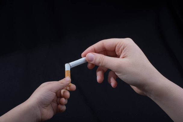 Рука разбивает сигарету на черном фоне - Фото, изображение