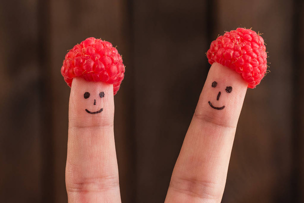 Two smiling faces drawn on fingers in caps from raspberry - Photo, Image