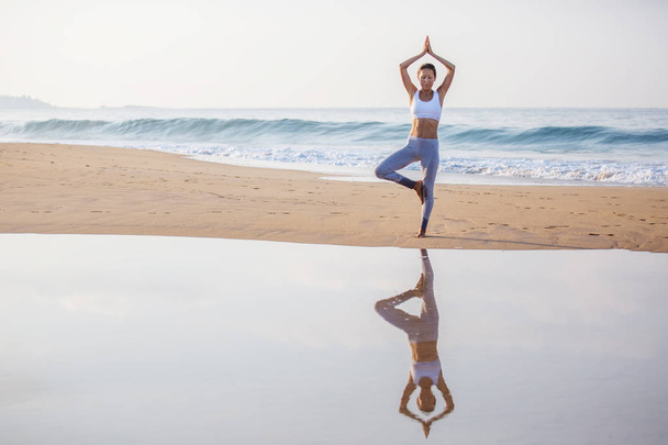 Caucasian woman practicing yoga at seashore of tropic ocean - Fotó, kép