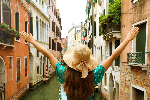 Woman traveler with straw hat and arms raised on bridge in Venice. Back view of fashion woman with open arms beautiful Venice channel on the background. - Foto, imagen