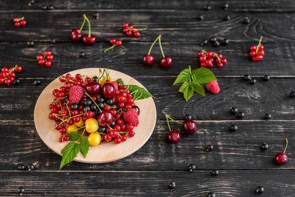 Raspberry, cherry, red currant, blackcurrant on a wooden plate against a dark background. It can be used as a background - Foto, afbeelding