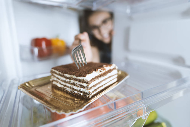 Hungry woman eating a dessert straight from the fridge using a fork, diet fail concept - Фото, зображення