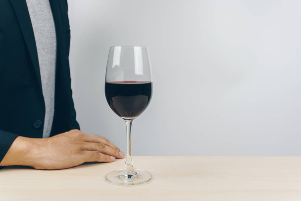 a glass of red wine on the wooden table, man in grey shirt and black suit in the background - Foto, afbeelding