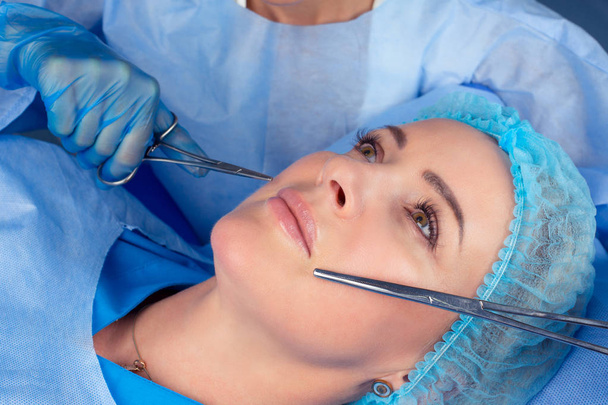 Close up of hands of cosmetologist preparing for lip surgery holding tools near in female mouth. She is holding tweezers and scissors. The mature beautiful woman is receiving procedure with enjoyment - Fotoğraf, Görsel