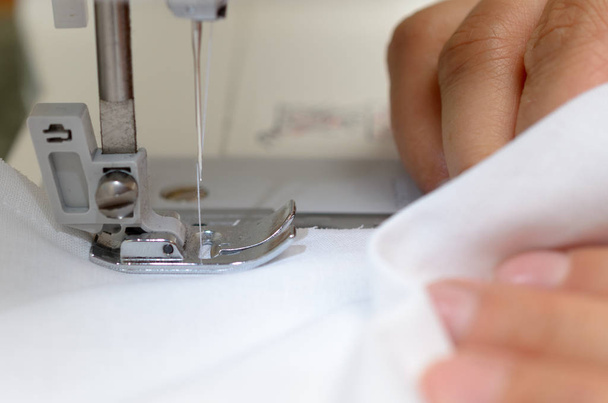 Manos costureras con material blanco detrás de la máquina de coser
. - Foto, imagen