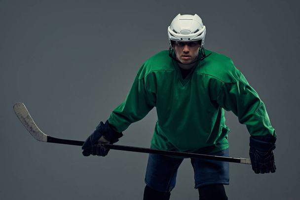 Portret van een professioneel hockeyspeler dragen van volledige versnelling en hockey stick. Geïsoleerd op een grijze achtergrond. - Foto, afbeelding