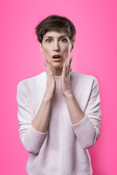 Женский портрет в пол-метра поверх розового студийного задника. Молодая эмоциональная улыбающаяся и удивленная женщина, стоящая и смотрящая в камеру
. - Фото, изображение