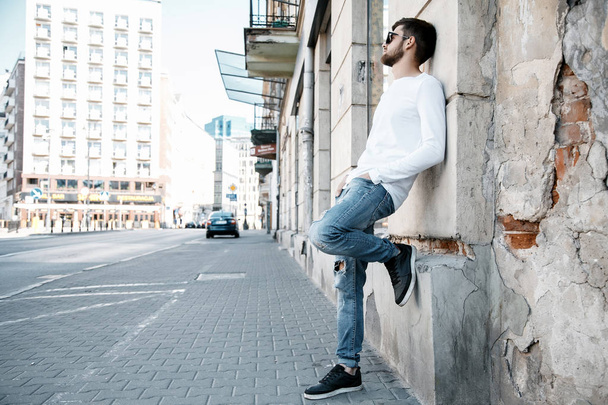 A young man travels through the streets of the city. Boy in sunglasses Stylish man near the building. The man sits on a whip. Beard and hair in a stylish guy. Senior student after studying. - Foto, Imagem