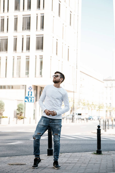A young man travels through the streets of the city. Boy in sunglasses Stylish man near the building. The man sits on a whip. Beard and hair in a stylish guy. Senior student after studying. - 写真・画像