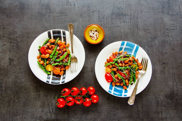 Vegan bonen salade met asperges, micro Groenen en tomaten plat leggen. Gezonde energie boost salade in platen op donkere achtergrond. Schoon eten, superfood, veganistisch, detox van voedselveiligheid concept. Bovenaanzicht - Foto, afbeelding