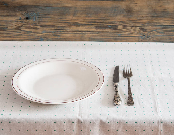 White empty plate with vintage silver ware fork and knife on a polka dot tableclot - Fotó, kép