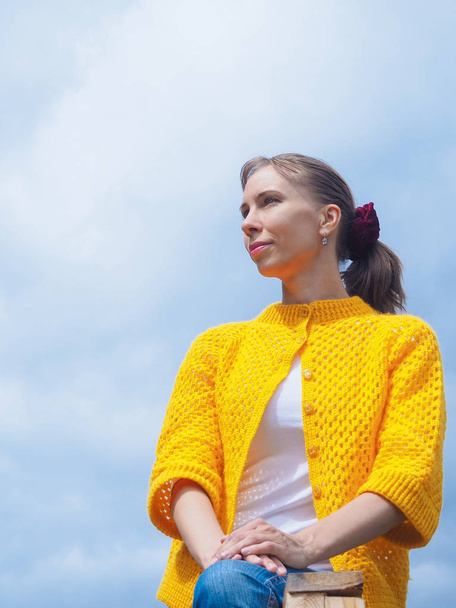 Woman in yellow knitted sweater sitting on a sky background. - Photo, Image