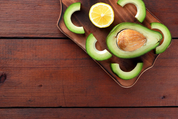 Avocado on wooden board top view, sliced avocado and lemon on wooden boards, vegetarian food, wholesome asian food, tropical fruits for breakfast, Mexican food, copy space - Foto, Bild