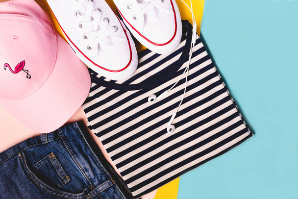 Концепция блогера моды. Летний спорт, отдых и туристический костюм: полосатая футболка, джинсовые шорты, розовая шляпа, белые сникеры. Минимальный набор женской одежды подростка на пастельном фоне
. - Фото, изображение