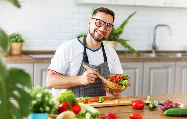 happy  man preparing vegetable salad in the kitche - Photo, Image