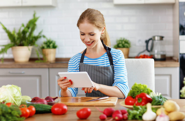 onnellinen nainen valmistelee vihanneksia keittiössä reseptillä pöydällä
 - Valokuva, kuva