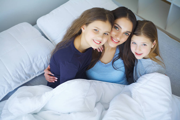 Lachende Kinder, die mit ihrer Mutter spielen, die auf einem Bett liegt - Foto, Bild
