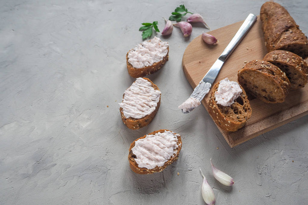 Σνακ με κρέμα σκόρδο σε φέτες ολικής αλέσεως μπαγκέτα σε φόντο γκρι τσιμέντο. - Φωτογραφία, εικόνα
