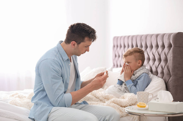 Father taking care of little son suffering from cold in bed - Foto, Imagen
