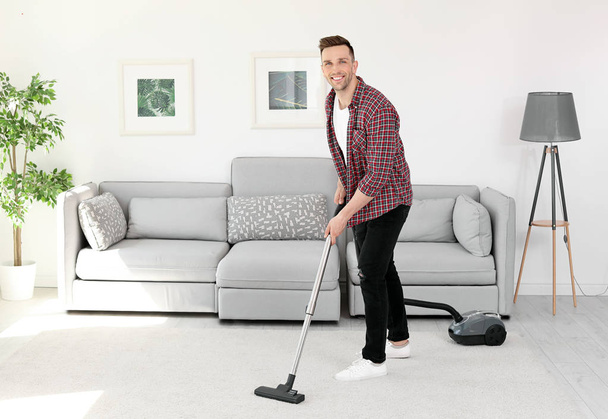 Young man removing dirt from carpet with vacuum cleaner at home - Photo, Image