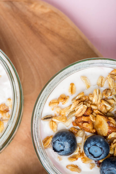 Breakfast from Fresh Natural Yogurt with Homemade Granola and Blueberries in Glass Jars on Light Pink Background - Photo, Image