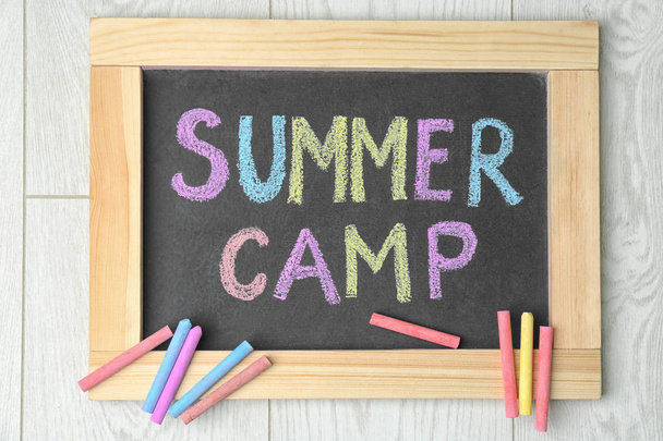 Blackboard with text SUMMER CAMP chalked in different colors on wooden background, top view - Foto, imagen