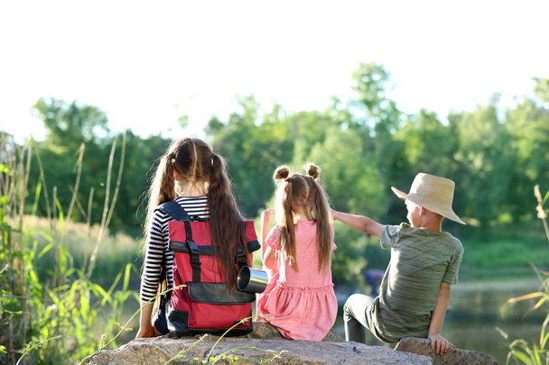 Little children sitting on rock outdoors. Summer camp - Zdjęcie, obraz